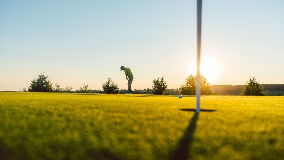Full length view of the silhouette of a male player, hitting a long shot on the putting green of a professional golf course of a modern country club