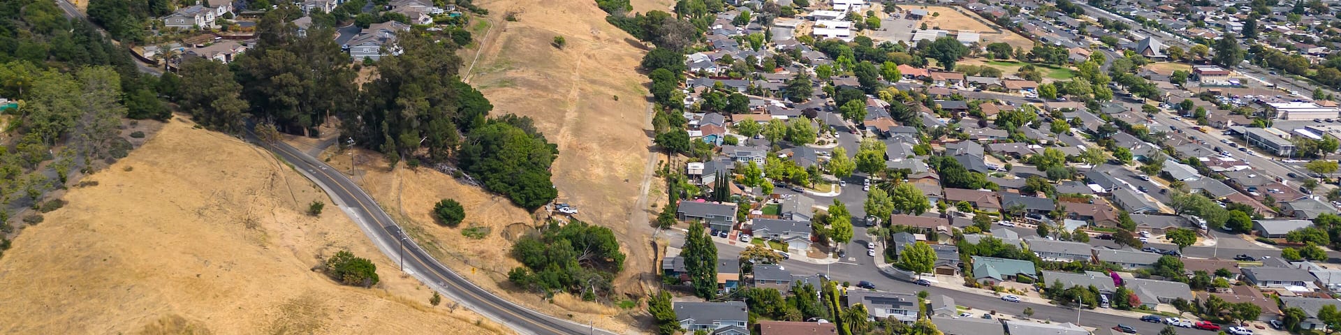 An aerial view of a residential area with houses, roads, and rolling hills.