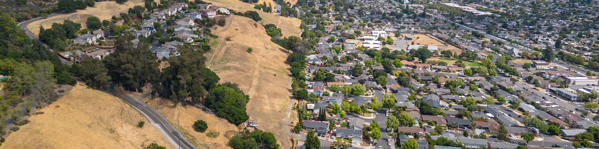 Vue aérienne d’un quartier résidentiel avec des maisons, des routes et des collines ondulantes.