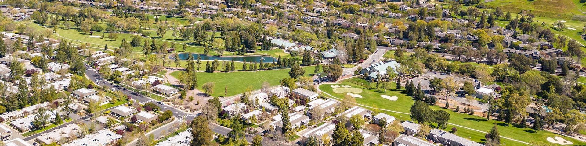 A stunning drone photo captures the Rossmoor community's picturesque beauty, showcasing homes, a golf course, green hills, and a clear blue sky.