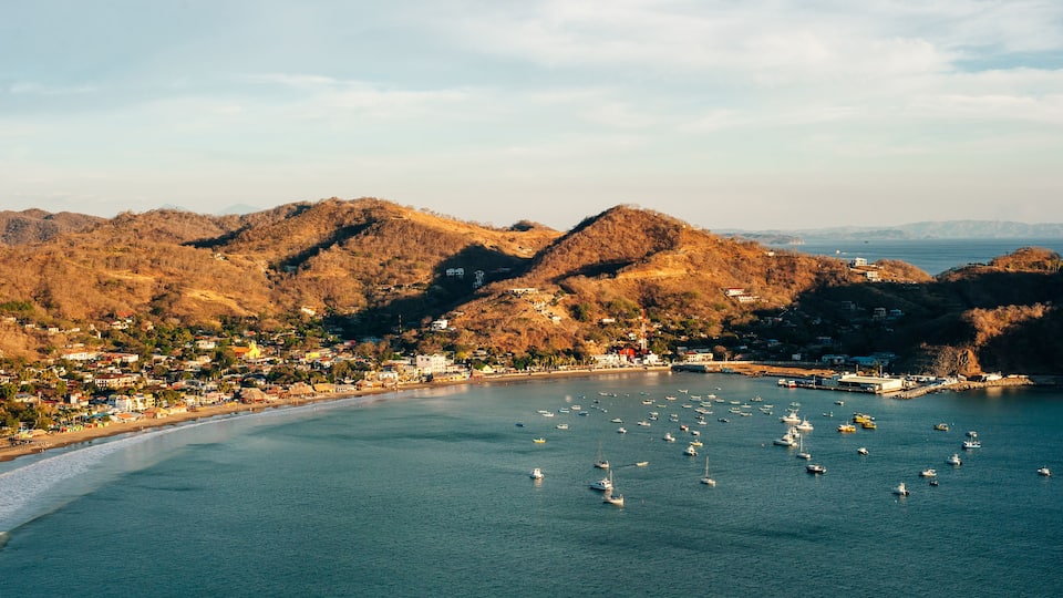 Un pueblo costero con una bahía llena de barcos, rodeado de colinas.