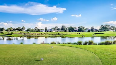 A golf course with a pond, green hills, and a clear sky.