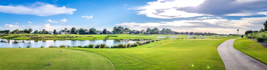 A golf course with a pond, green hills, and a clear sky.