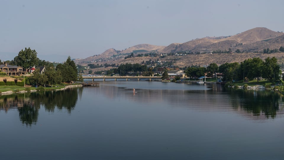 Lake Chelan panoramic landscape on a beautiful summer day, showing the lake, trees and greenery and the arid brown hills in the background.