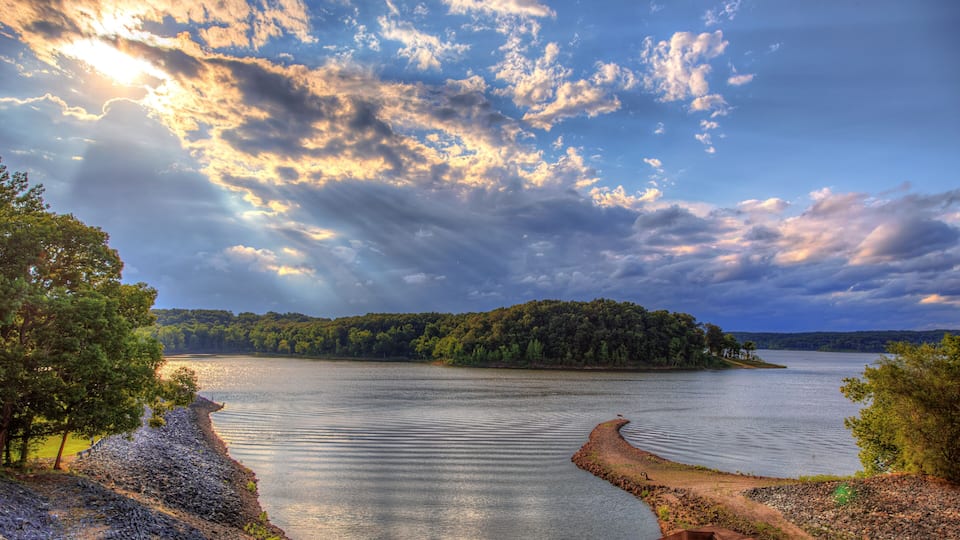 A calm lake with a wooden dock, surrounded by trees and a forested island.