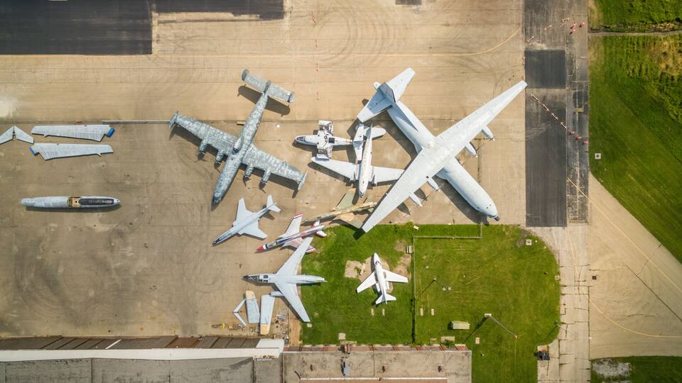 An aerial view of an airport with multiple aircraft parked on the tarmac, including large commercial jets and smaller planes.