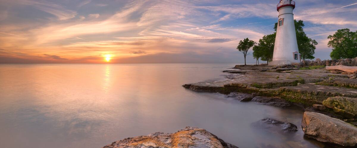 A lighthouse on a rocky shore at sunset.