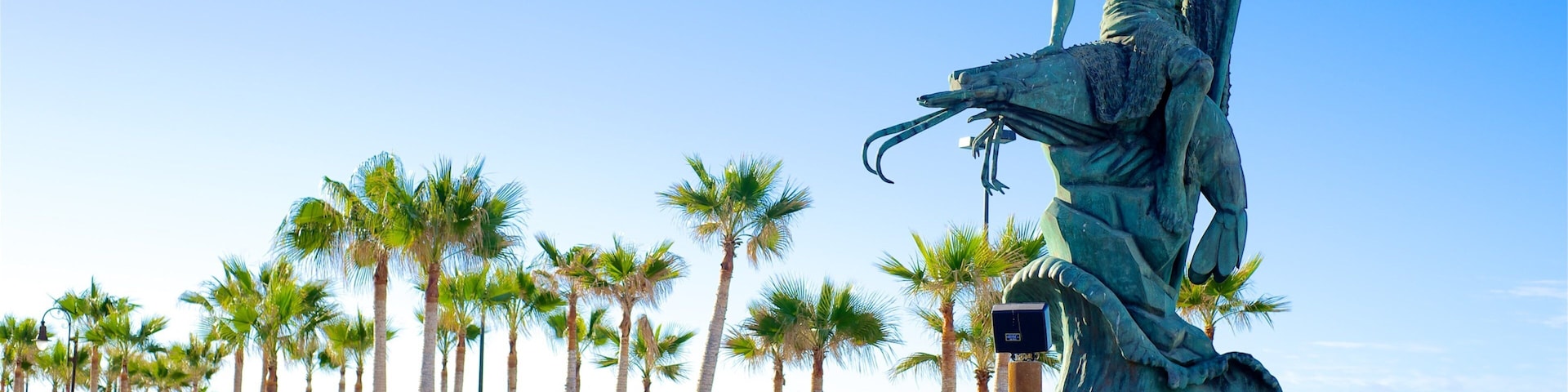 A statue of a woman with a spear on a pedestal, palm trees, and a beach in the background.