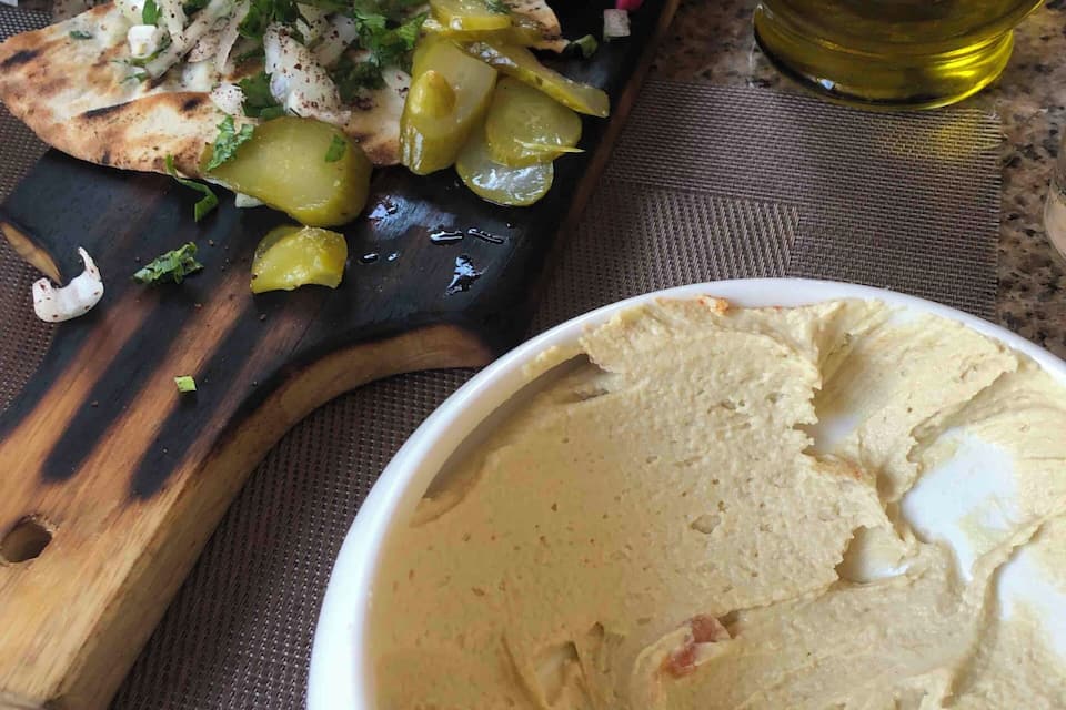 Una comida con verduras a la parrilla, un tazón de hummus y una botella de aceite de oliva sobre una mesa.