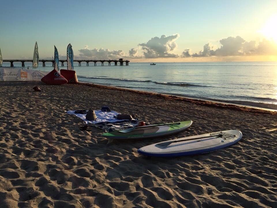 A beach with surfboards, a pier, and a sunset.