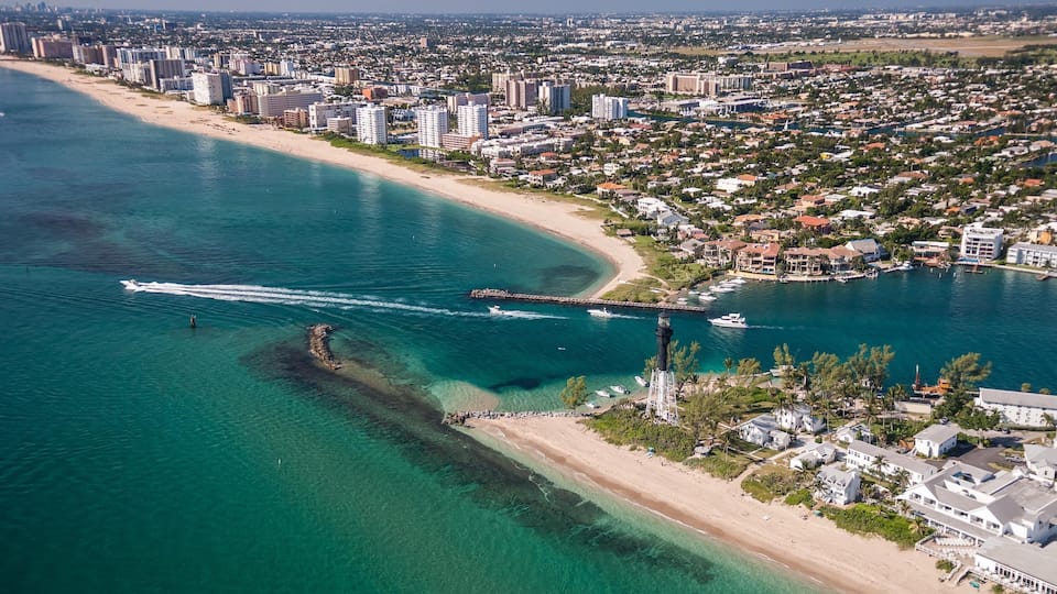 An aerial view of a coastal city with a beach, clear blue waters, and a lighthouse.