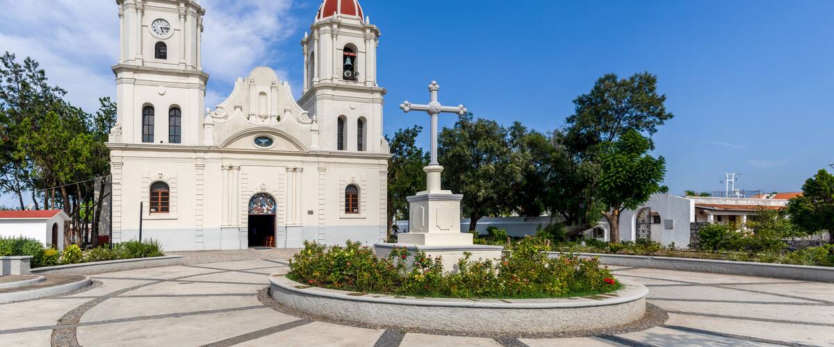A white church with two red domes and a cross statue in front.