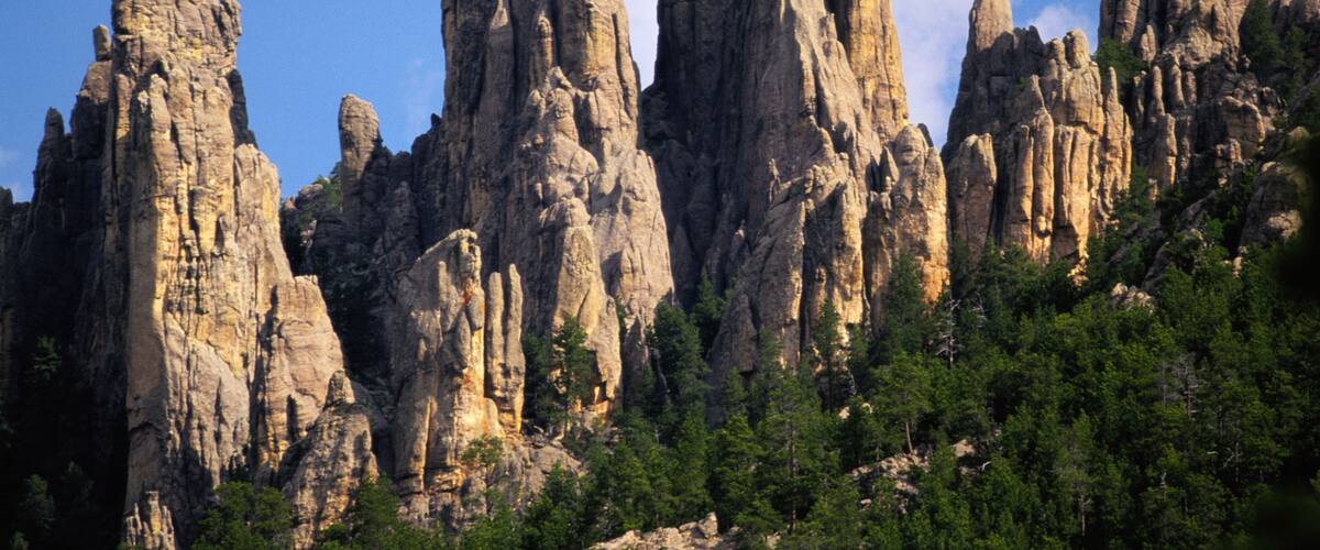 A rugged mountain range with prominent rock formations and dense green forest at its base.