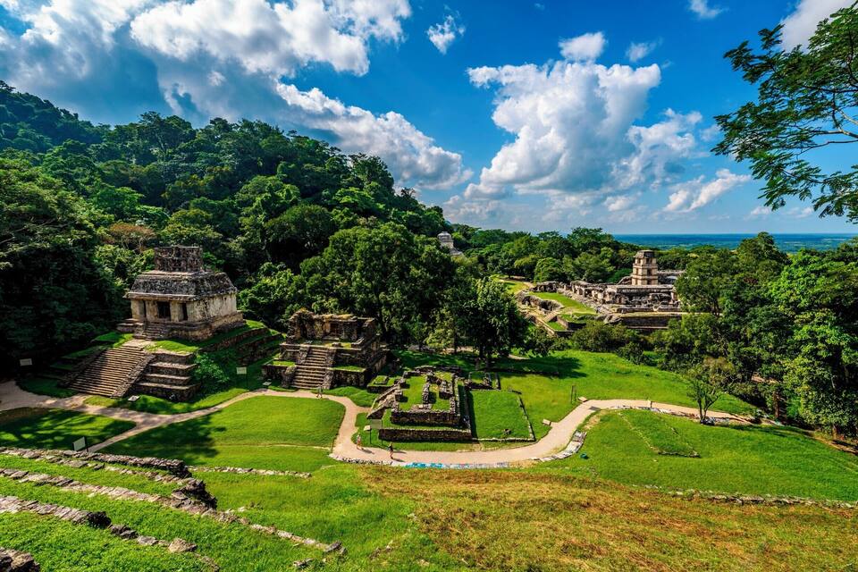 Ruinas antiguas rodeadas de vegetación exuberante y un cielo azul despejado.