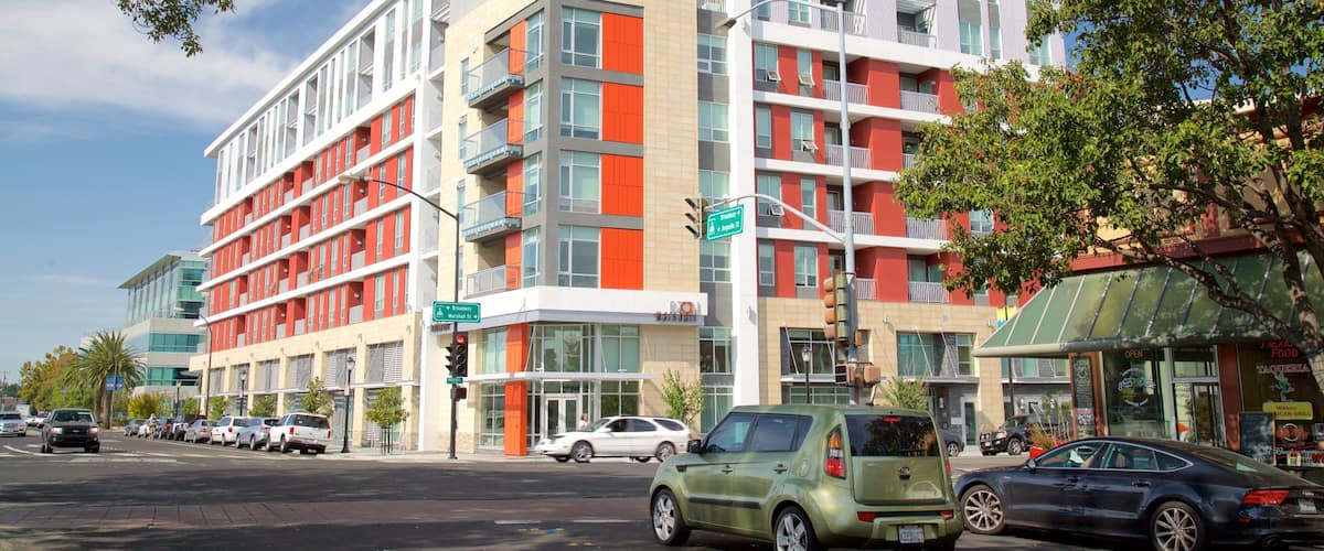 A modern multi-story building with red and white accents, located at a street corner with visible street signs and parked cars.