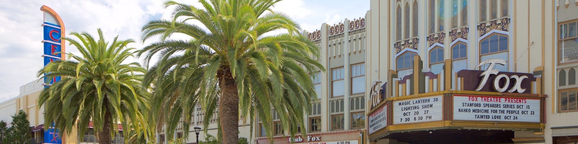 Um teatro com palmeiras na frente, uma placa de pare e um carro azul na rua.