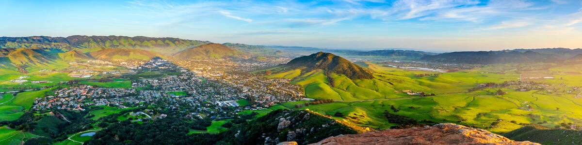 A mountainous landscape with a town nestled in the valley, a prominent hill, and a river flowing through the scene.