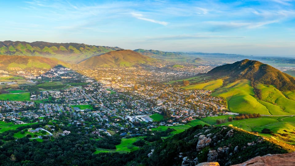 A mountainous landscape with a town nestled in the valley, a prominent hill, and a river flowing through the scene.