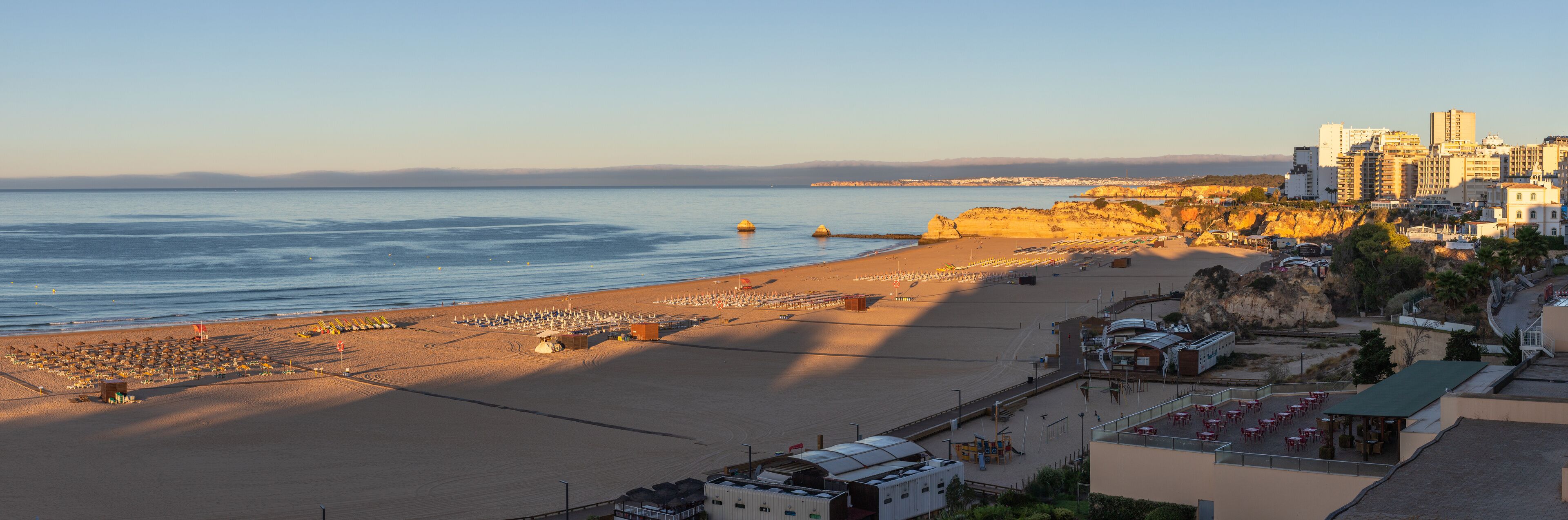 A coastal cityscape with a wide beach, rocky cliffs, and modern buildings.