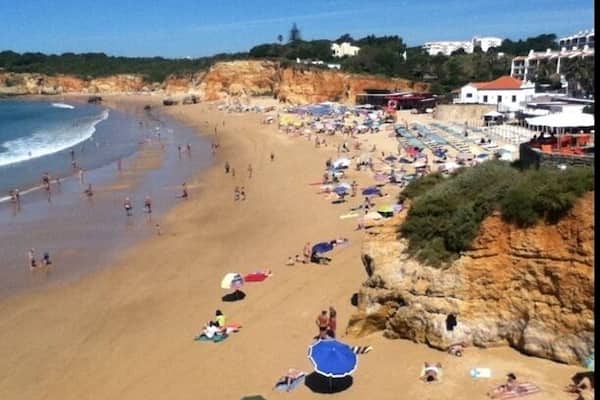 Ein Strand mit badenden Personen, Sonnenschirmen und einer felsigen Klippe.
