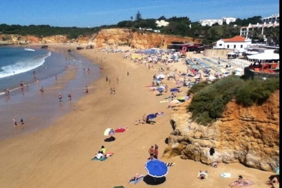 Een strand met mensen die zonnebaden, parasols en een rotsachtige klif.