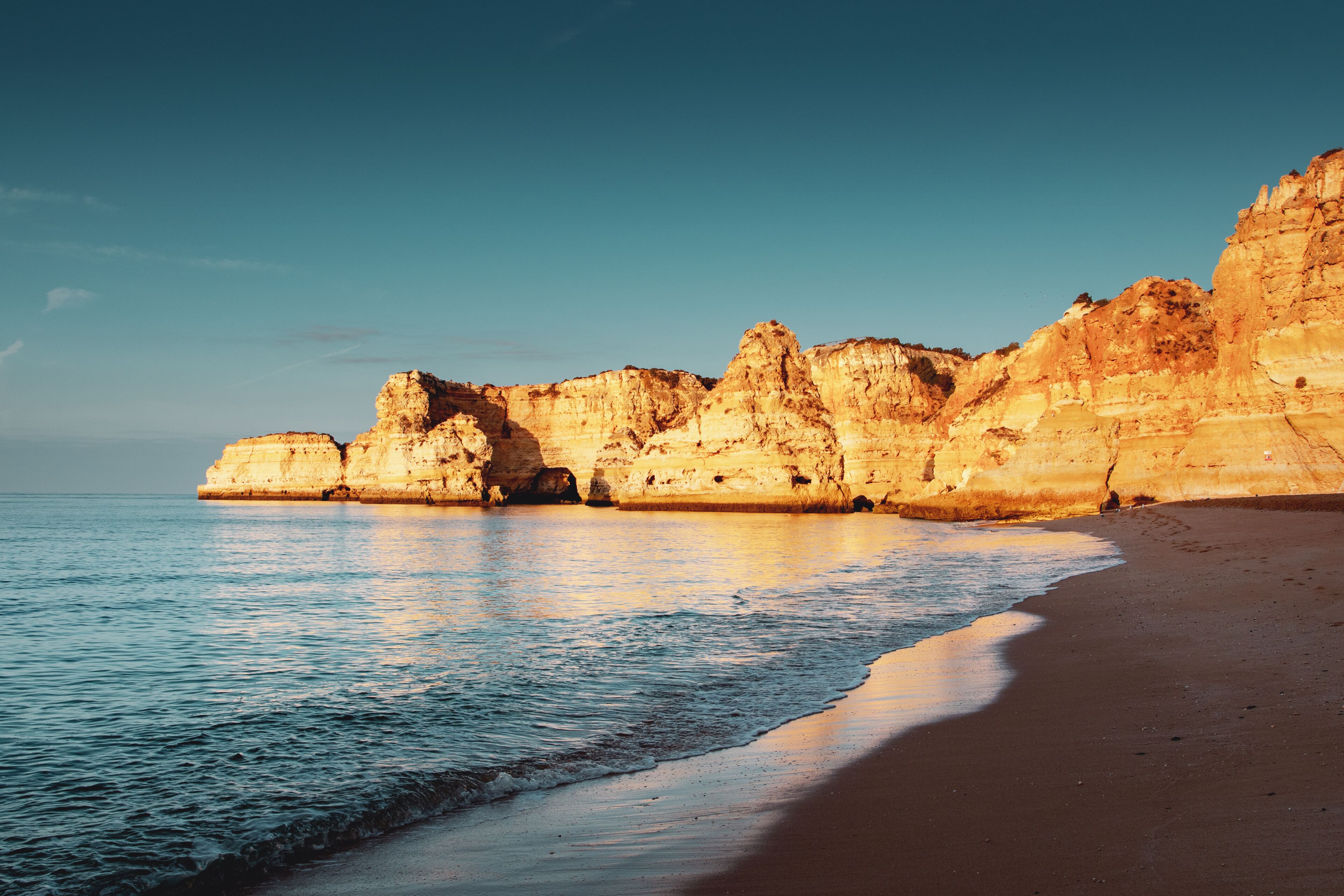A coastal landscape with a sandy beach and towering limestone cliffs.