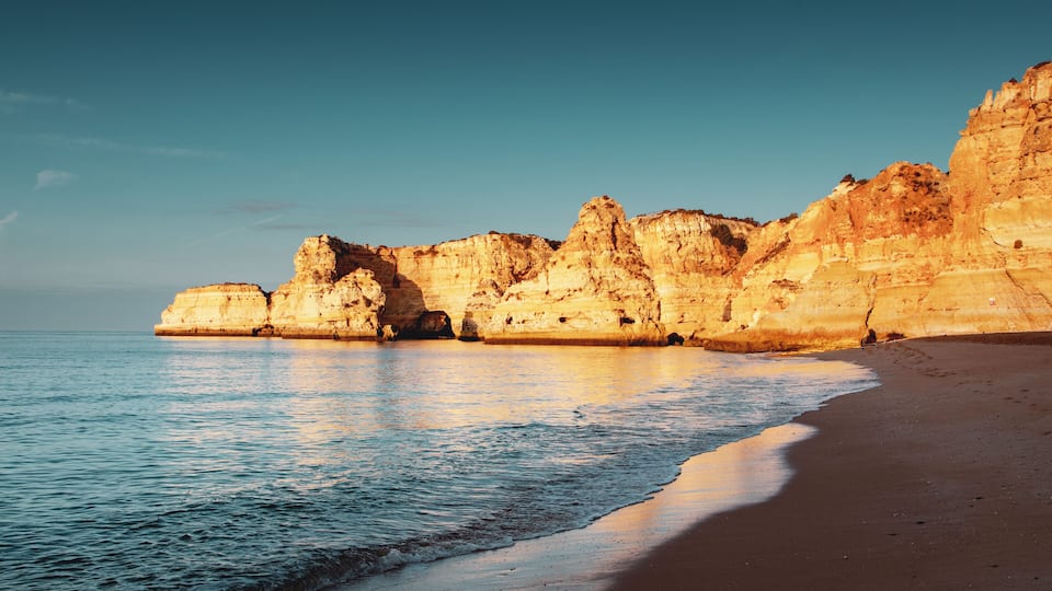 A coastal landscape with a sandy beach and towering limestone cliffs.