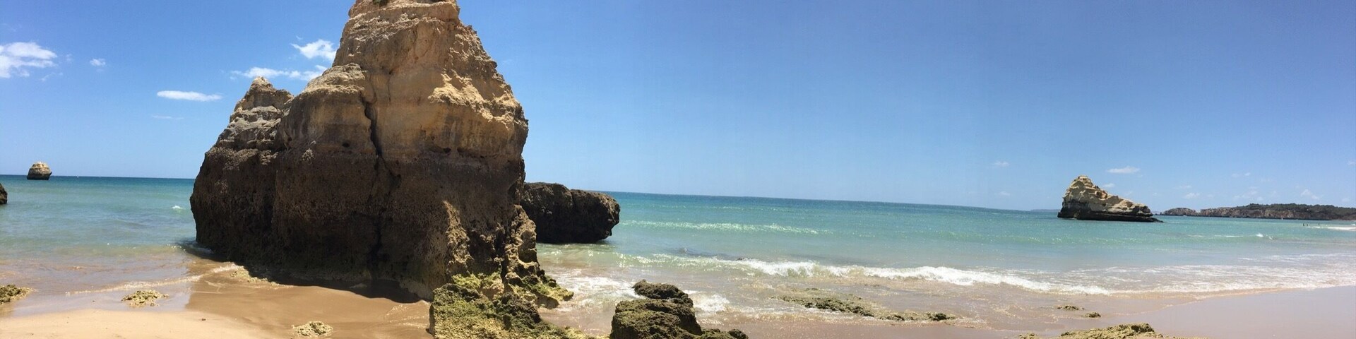 Une plage de sable fin, parsemée de grandes formations rocheuses, bordée par une mer calme.