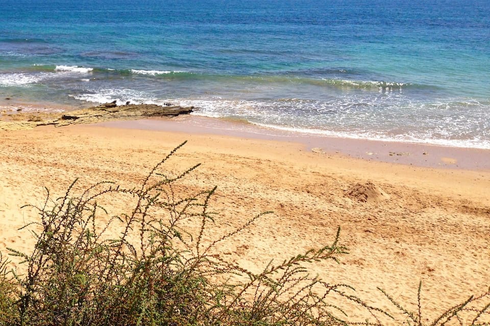 A sandy beach with gentle waves and clear blue water.