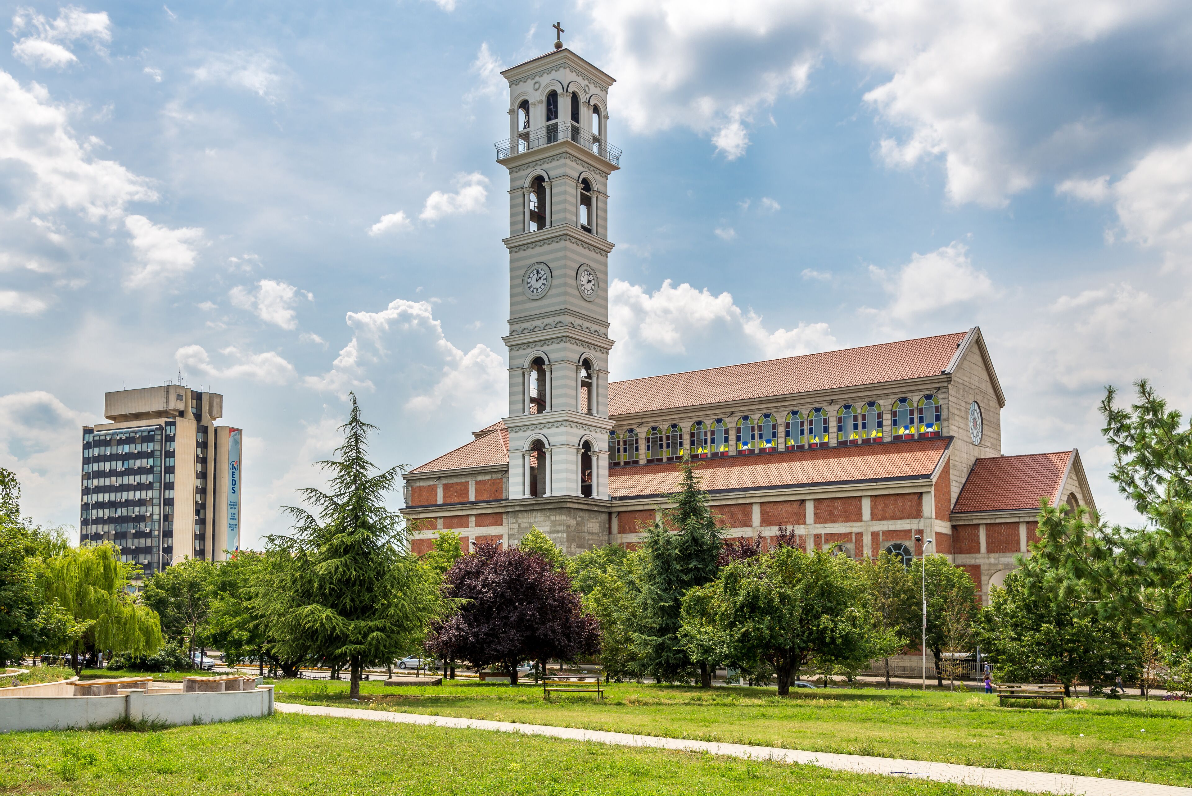 A historic church with a tall bell tower, surrounded by a grassy park and modern buildings.