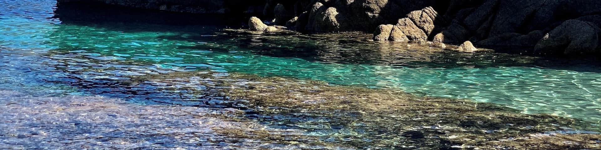 A lighthouse with a green top, a stone wall, and clear blue water.