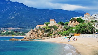 A coastal town with a beach, rocky cliffs, and a mountain in the background.