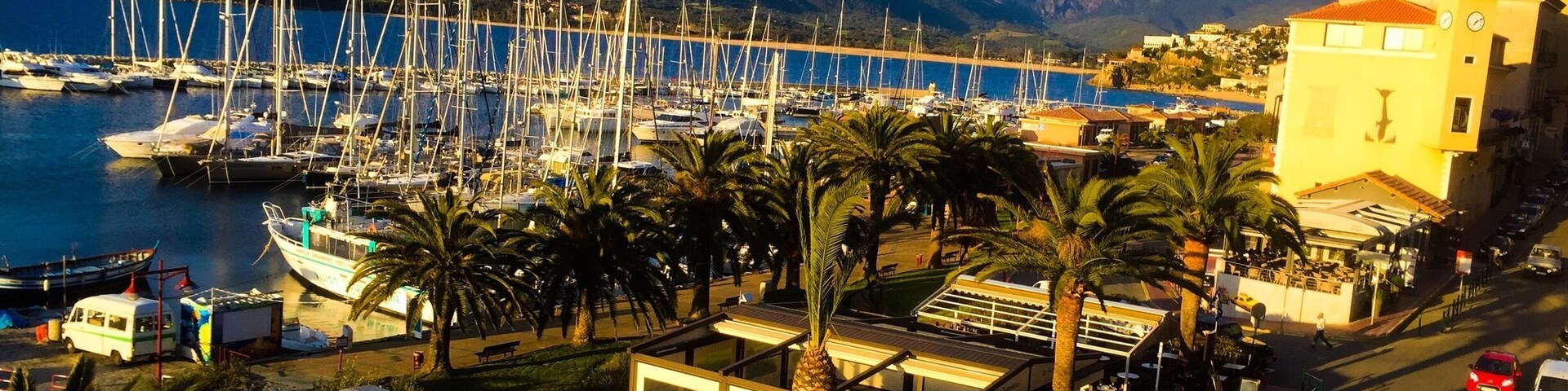 Una marina con barcos, un restaurante, palmeras y montañas al fondo.
