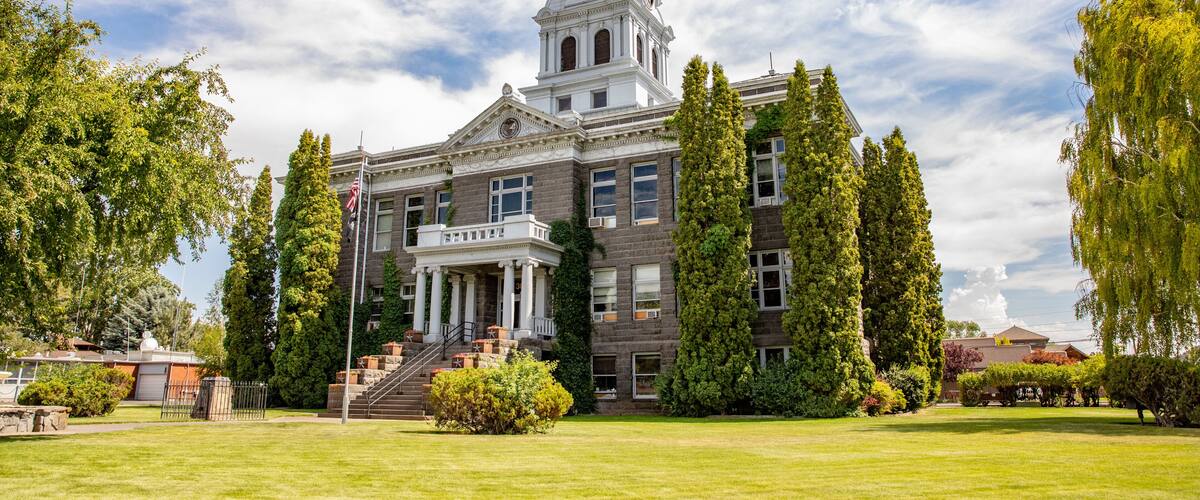 A historic building with a prominent clock tower, surrounded by well-maintained lawns and tall trees.