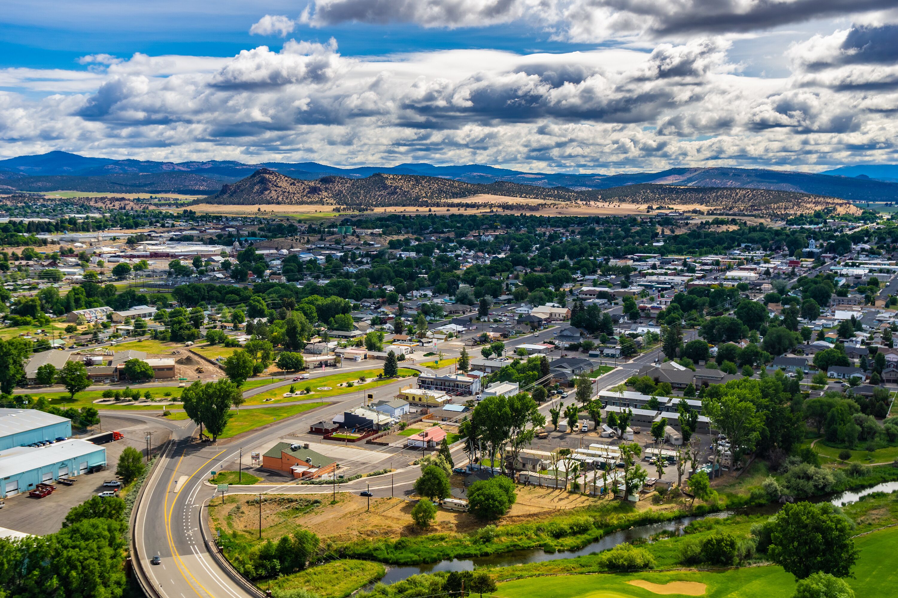 A town with a river, green fields, and mountains in the background.