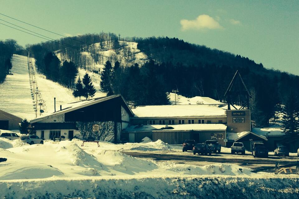 Un pueblo cubierto de nieve con edificios, un telesilla y una montaña al fondo.