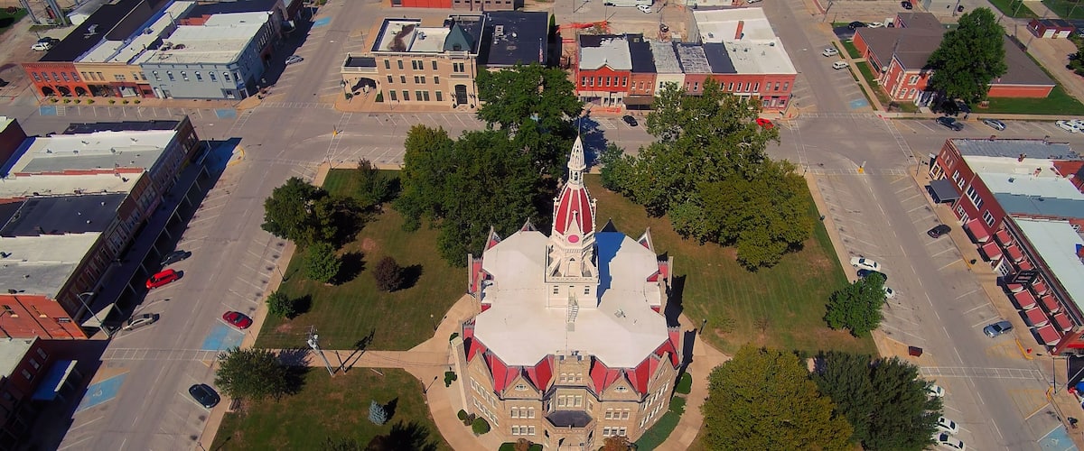An aerial view of a town with a prominent church featuring a red and white steeple, surrounded by green spaces and intersecting roads.