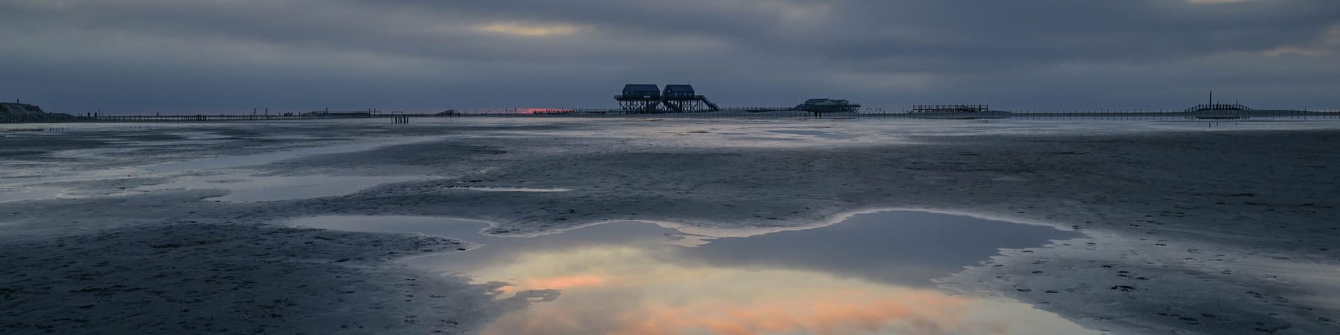 Landscape view of a beach and stilt houses with cloud reflexion in mud flat, St Peter-Ording, North Friesland, Germany, Europe.