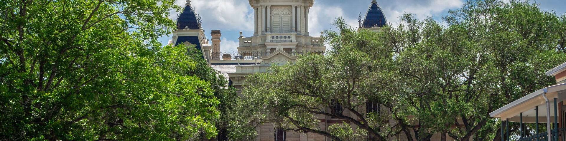 A historic building with a clock tower, parked cars, and trees.