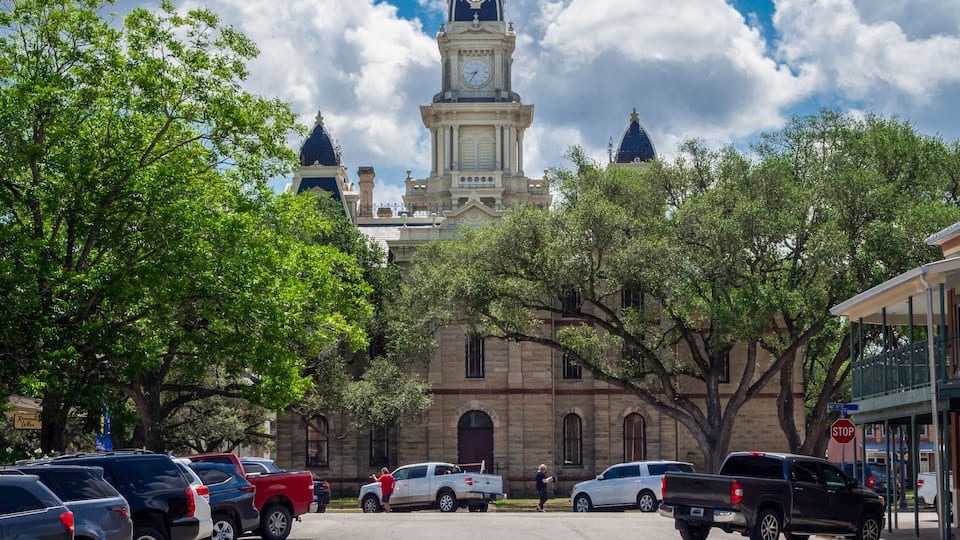A historic building with a clock tower, parked cars, and trees.