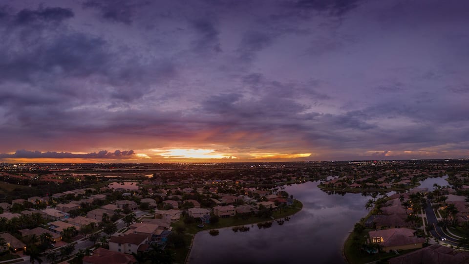 A sunset over a residential area with a river and houses.