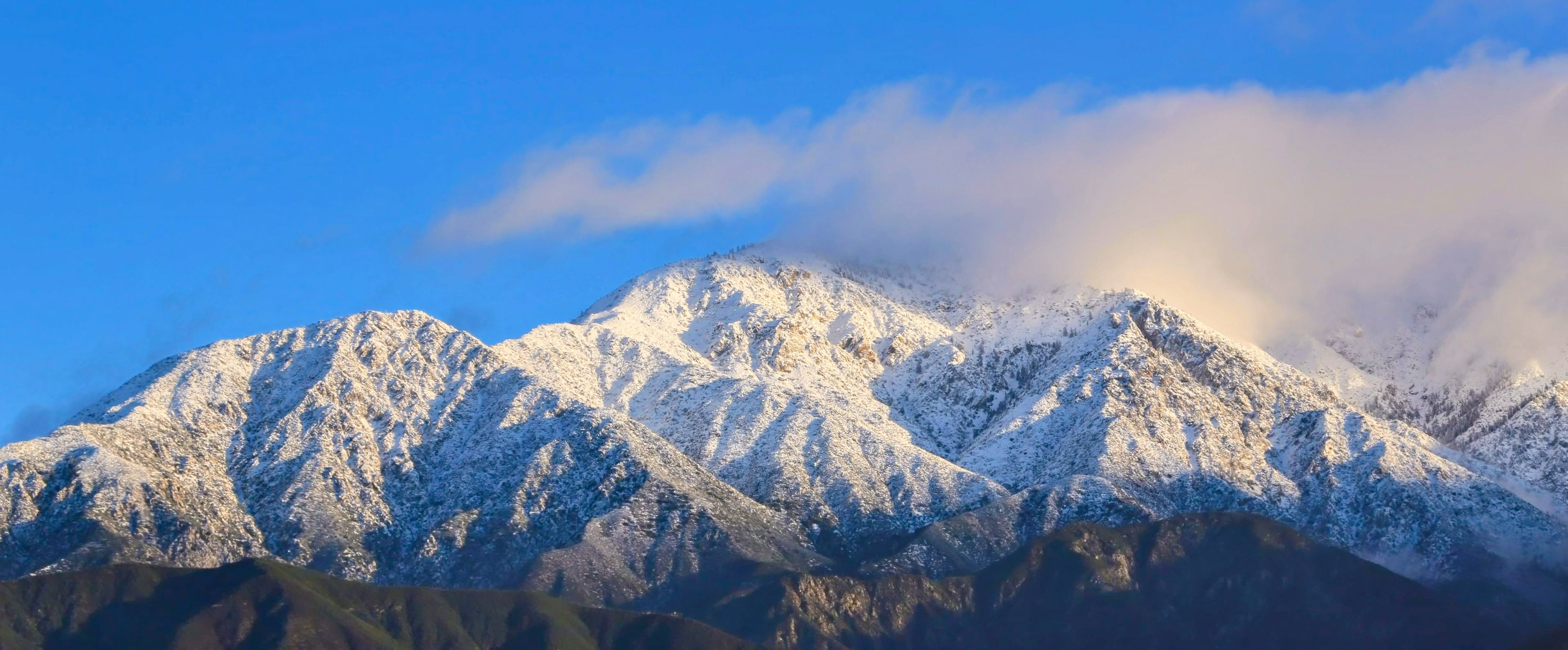 Picos nevados de montañas con cielo azul despejado y nubes.