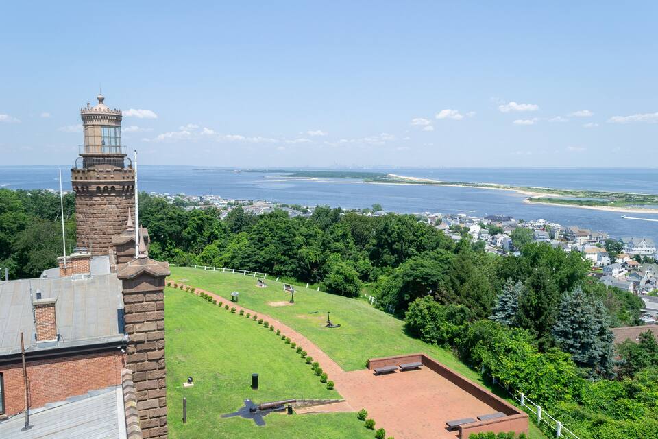 Vista costeira com um farol, áreas verdes e uma praia.