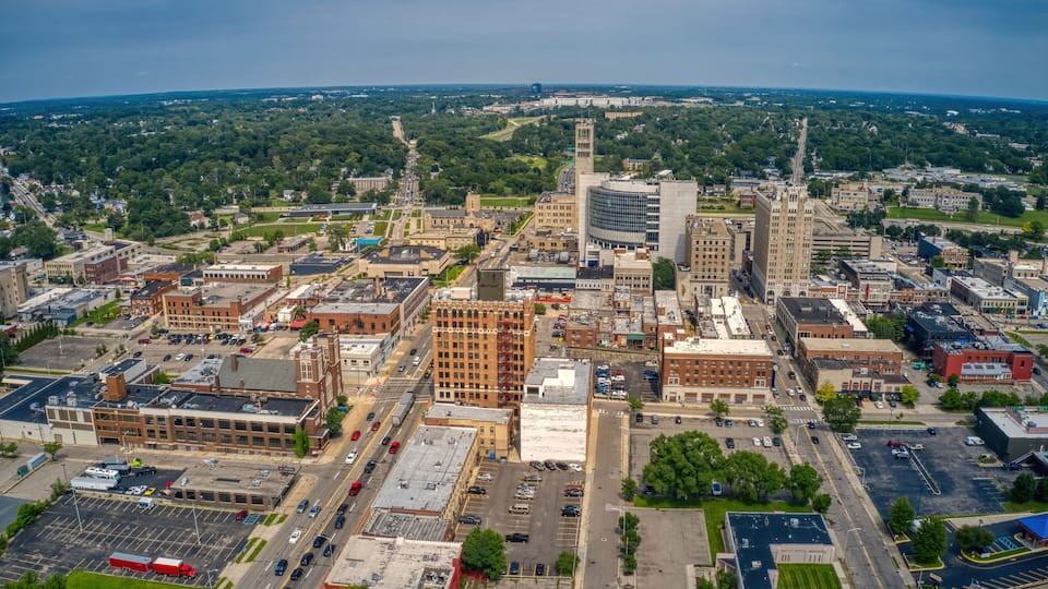 An aerial view of a city with a mix of historic and modern buildings, a prominent clock tower, and a large parking lot.