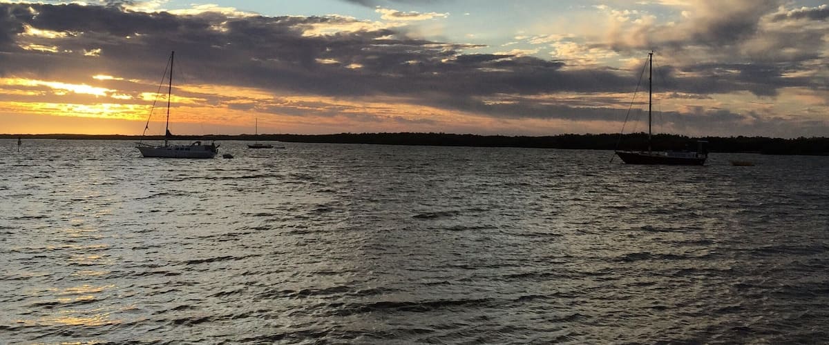 A sunset over a calm sea with sailboats and a beach.