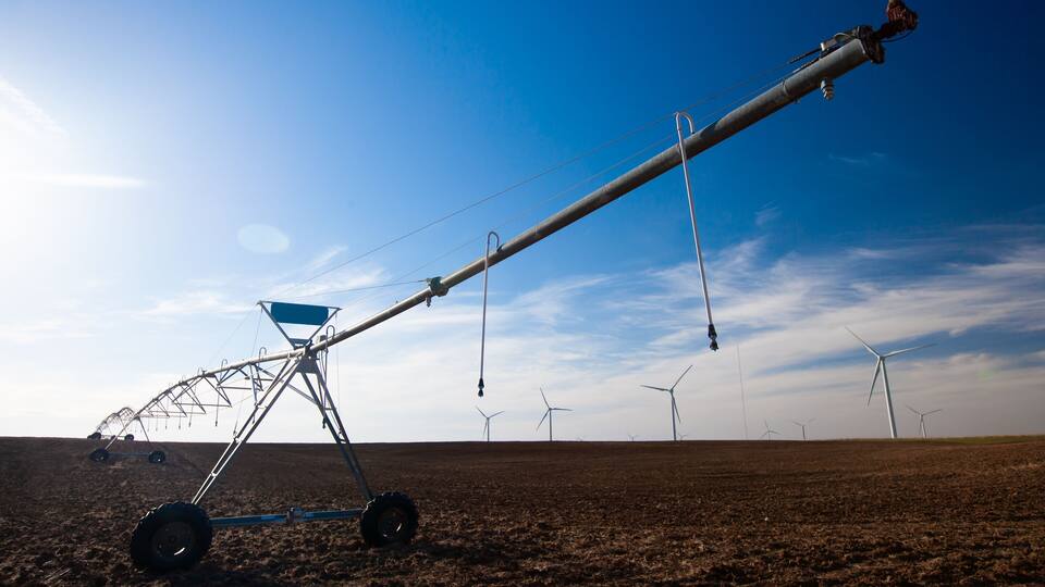 A large agricultural irrigation system in a field with wind turbines in the background.