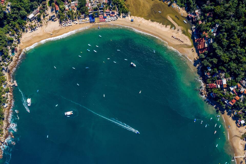 Une vue aérienne d’une zone côtière avec une plage, des bateaux et des bâtiments.