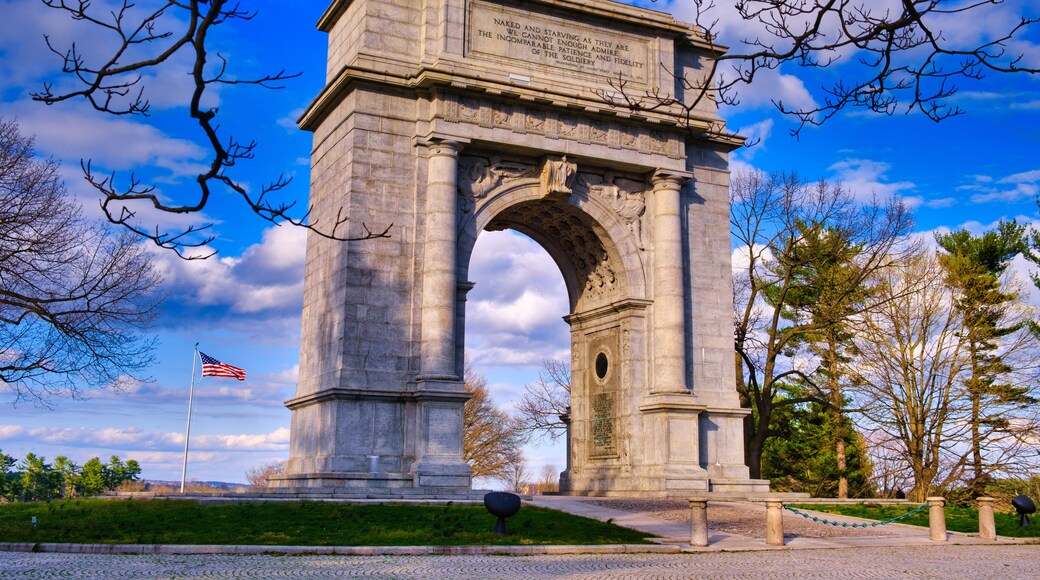 The National Memorial Arch stands with the American Flag blowing in the wind to the left at Valley Forge National Park in Pennsylvania.