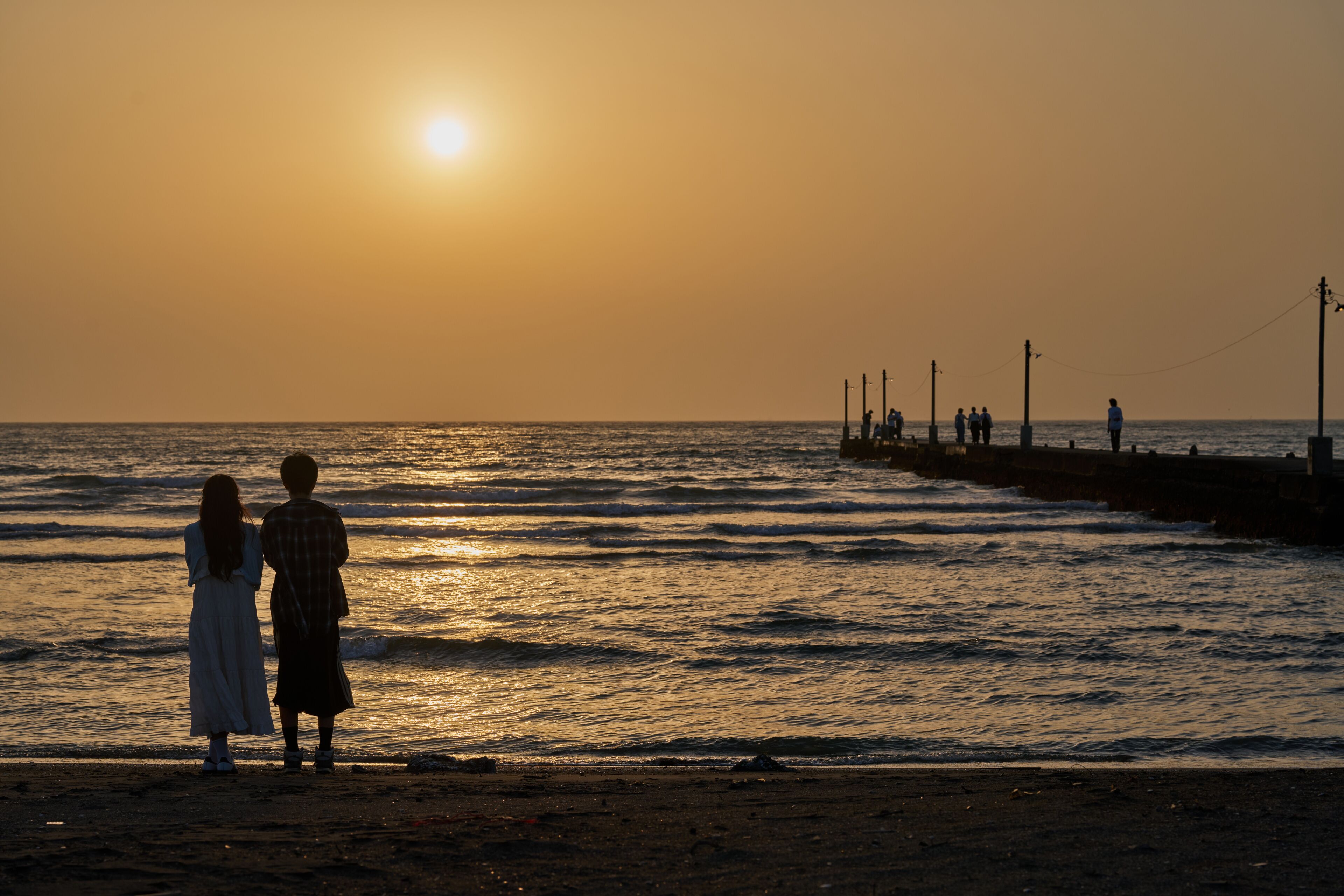 Un atardecer sobre el océano con un muelle y gente allí.
