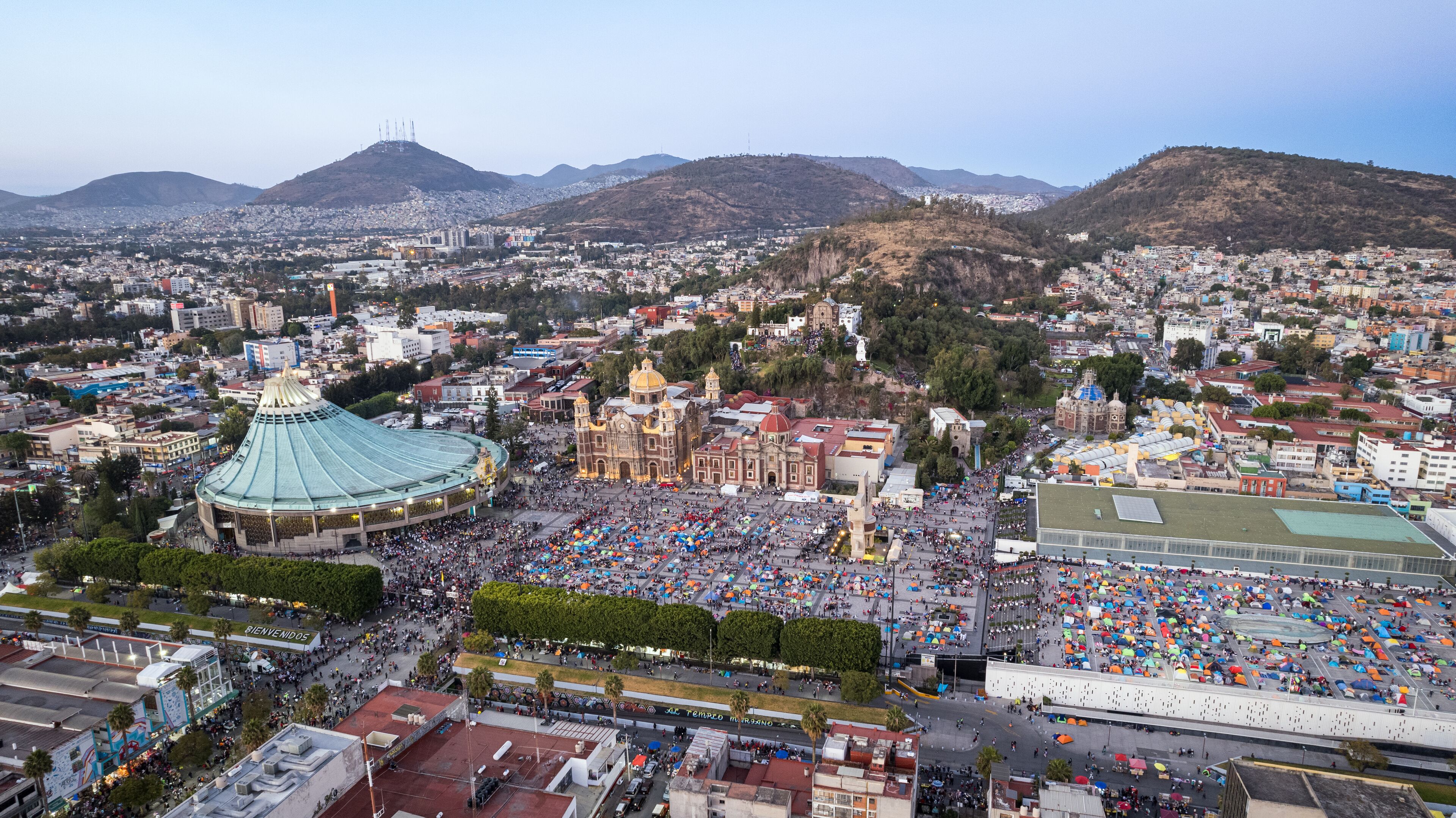 A cityscape with a large stadium, historic buildings, and a mountainous backdrop.